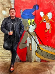 Мужчина нарисованный во весь рост в стиле Под масло, на фоне красной стены нарисован Том и Джерри, Том держит в руках барабан, художник Анна