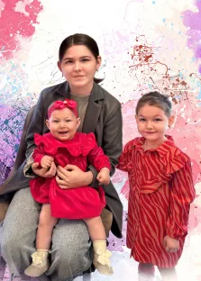 Семейный портрет в стиле бьюти. На портрете изображена женщина в сером пиджаке и брюках, держащая на коленях малышку в ярко-розовом платье с рюшами и ободочком с бантом; малышка радостно улыбается. Рядом стоит девочка постарше в красном платье с зебровым принтом и рюшами, с аккуратной причёской — обе девочки смотрят в камеру с лёгкими улыбками. Фон выполнен в абстрактной технике с брызгами краски в розовых, фиолетовых и голубых тонах, создавая жизнерадостную и динамичную атмосферу. Художник: Артём