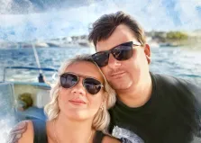 На изображении запечатлена пара, стоящая близко друг к другу, на фоне морского пейзажа. У женщины светлые, волнистые волосы до плеч, она носит солнцезащитные очки-авиаторы с металлическими оправами. 
 Акварель, художник Анна М