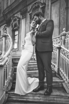 Парный портрет в стиле карандаш. На чёрно-белой фотографии изображена пара — жених в строгом костюме и невеста в элегантном длинном белом платье — стоящая на лестнице старинного здания. Жених нежно обнимает невесту, склонившись к её лицу, создавая атмосферу трогательной близости и романтики. Художник Антонина