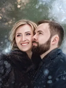Парный портрет под масло. На портрете изображена влюблённая пара: женщина с светлыми волосами в тёмной шубе тепло улыбается, а мужчина с бородой в чёрном костюме нежно прижимается к её щеке. Вокруг них кружатся снежинки, а размытый фон с мягкими световыми бликами создаёт атмосферу зимнего уюта и романтики. Художник: Александра 
