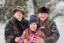 Семейный портрет под масло. На портрете изображена семья из трёх человек — пожилая женщина в тёмной шубе и меховой шапке, мужчина в тёплой куртке с меховым воротником и пушистой шапке, а также улыбающаяся девочка в яркой розовой куртке и фиолетовой вязаной шапке. Все они стоят на фоне заснеженного леса, вокруг кружатся снежинки, создавая атмосферу зимнего уюта и семейного тепла. Художник: Александра 