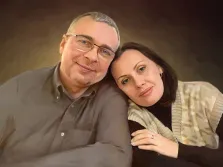 Под масло, художник Анастасия К На изображении представлен портрет пары, выполненный в живописном стиле. Задний фон имеет тёмно-коричневый оттенок.
Мужчина находится слева. У него короткие седые волосы и щетина. На нём надета рубашка цвета хаки с застегнутыми пуговицами. Он также носит очки с прозрачными линзами и тонкой металлической оправой. Под масло, художник Анастасия К