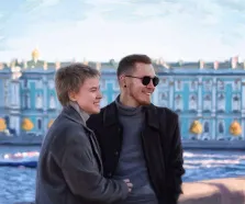 Парный портрет под масло. На картине изображены двое улыбающихся людей, стоящих рядом на фоне Зимнего Дворца, это один из дворцов Санкт-Петербурга. Атмосфера тёплая и радостная: оба персонажа выглядят расслабленно и счастливо, наслаждаясь моментом. Художник Александра.