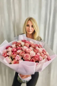 Женский портрет под масло. На картине изображена женщина с длинными светлыми волосами, одетая в тёмную одежду, которая держит в руках большой пышный букет розовых и кремовых роз, аккуратно упакованный в светло-розовую бумагу. Фон выполнен в виде нейтральных светлых вертикальных мазков, создающих спокойную и элегантную атмосферу. Художник Александра