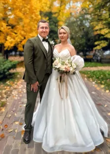 Парный портрет под масло. На картине изображена свадебная пара: жених в элегантном тёмно-оливковом костюме с бабочкой и невеста в пышном белом платье с открытыми плечами, держащая букет из нежных пастельных цветов. Они стоят на аллее, усыпанной осенними листьями, на фоне ярких жёлтых деревьев, создавая атмосферу уюта и торжества. Художник Александра 