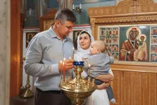 Семейный портрет в стиле под масло. На картине изображена семья в интерьере православного храма: мужчина зажигает свечи на золотом подсвечнике, рядом с ним женщина в белом платке держит на руках малыша. На заднем плане видны иконы и резной иконостас, создающие торжественную и благоговейную атмосферу. Художник Ирина