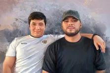 Мужской портрет в стиле под масло. На картине изображены двое мужчин: один в белой футболке с надписью «RUSSIA» и гербом, с лёгкой улыбкой на лице, другой — в чёрной футболке и кепке с надписью «GUESS», с серьёзным выражением лица. Мужчина в белой футболке положил руку на плечо своего спутника, что создаёт ощущение дружеской близости на фоне абстрактного серо-золотистого фона. Художник Анна 