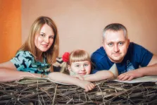 Семейный портрет в стиле под масло. На картине изображён семейный портрет: женщина в голубой блузке с чёрным узором, мужчина в синей футболке и маленькая девочка с красным бантом в волосах. Все трое опираются на конструкцию, напоминающую гнездо из веток, и смотрят прямо на зрителя с тёплыми, доброжелательными выражениями лиц. Художник Александра 