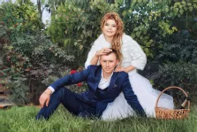 Парный портрет в стиле под масло. На картине изображена пара в свадебных нарядах: мужчина в тёмно-синем костюме сидит на траве, а женщина в белом платье и пушистой накидке нежно кладёт руку ему на голову. Рядом с ними стоит плетёная корзина с бутылкой шампанского, а на фоне — густая зелёная растительность с яркими красными ягодами. Художник Александра