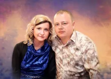 Парный портрет в стиле под масло. Женщина в синем бархатном платье с чёрным жакетом и светлыми волнистыми волосами стоит рядом с мужчиной в светлой рубашке с узором. Фон выполнен в мягких, размытых оттенках фиолетового и золотистого, создающих тёплую и гармоничную атмосферу. Художник Артём