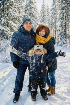 Семейный портрет в стиле под масло. На картине изображена счастливая семья из трёх человек — мужчина, женщина и ребёнок — на фоне заснеженного леса. Ребёнок в тёплой куртке и шапке с ушками радостно раскинул руки, вокруг него кружатся снежинки, а взрослые стоят позади с улыбками, наслаждаясь зимним днём. Художник Ирина