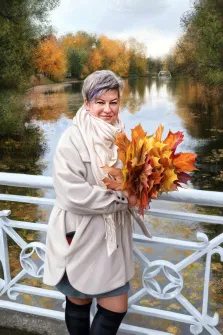 Женский портрет под масло. На портрете изображена женщина с короткими седыми волосами и яркой фиолетовой прядью, одетая в светлое пальто, объёмный шарф и чёрные сапоги; она тепло улыбается и держит в руках пышный букет осенних кленовых листьев. На фоне — живописный осенний пейзаж: спокойная река, мост с белыми перилами и деревья, окрашенные в золотисто-оранжевые тона. Художник: Артём