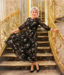 Женский портрет под масло. На портрете изображена улыбающаяся женщина с короткими седыми волосами, стоящая на роскошной лестнице с золотыми перилами. Она одета в элегантное чёрное платье с цветочным принтом, дополненное поясом и чёрными туфлями, и грациозно придерживает подол платья руками. Художник: Анна