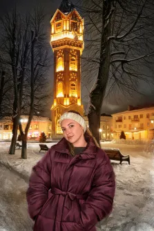 Женский портрет под масло. На портрете изображена молодая женщина в объёмной бордовой пуховой куртке и светлой вязаной шапке, стоящая на заснеженной улице; её поза расслаблена, а взгляд направлен прямо в камеру с лёгкой полуулыбкой. На фоне — величественная водонапорная башня, освещённая тёплым жёлтым светом, окружённая голыми зимними деревьями и заснеженными скамейками. Художник: Анна 