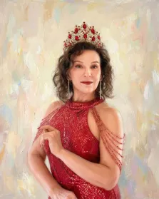 Женский портрет под масло. На портрете изображена женщина в роскошном красном платье с блестящими деталями и изящными нитями, спадающими с плеча; на голове у неё величественная корона, украшенная крупными красными камнями. Её поза элегантна, а выражение лица — спокойное и уверенное, фон выполнен в мягких пастельных тонах, подчёркивающих торжественность образа. Художник: Ирина