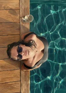 Женский портрет под масло. На портрете изображена женщина в чёрном купальнике и тёмных солнцезащитных очках, опирающаяся на край бассейна; её волосы мокрые и слегка растрёпаны. Рядом на деревянной поверхности стоит бокал с напитком, а прозрачная вода бассейна с игрой солнечных бликов создаёт атмосферу расслабленного летнего отдыха. Художник: Ирина