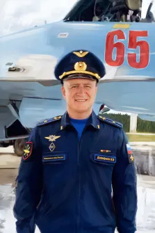 Мужской портрет в образе. На картине изображён офицер Вооружённых сил России в парадной форме с погонами и знаками отличия, на груди видны медали и нашивка с именем. На фоне — военный самолёт с ярко выделенным номером «65», создающий ощущение принадлежности героя к авиационной службе. Художник Анастасия