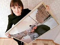 Женщина держит фотографию на холсте в бежевой багетной рамке с изображением ее и мужа.
