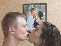 Молодой человек целует девушку перед фотографией на холсте, оформленном в багет, на которой запечатлен такой же их поцелуй.