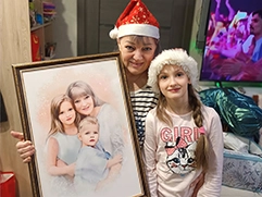 Бабушка с внучкой в шапочках Санта-Клауса рядом с подарком — портретом по фото на холсте в рамке, на котором изображены они и маленький мальчик