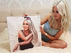 Девушка-блондинка, сидя на кровати, держит собственный портрет по фото на холсте