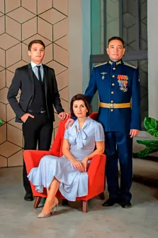 Семейный портрет на три персоны Под масло, слева молодой человек в чёрном классическом костюме, справа в синей военной форме с медалями, посередине сидит женщина в светлом платье на красном кресле, художник Анастасия 
