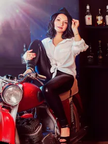 Кареглазая девушка в белой рубашке, чёрной шляпе и в чёрных лосинах сидит на красном мотоцикле, на фоне полки со спиртным, работа выполнена Под масло, художник Павел 