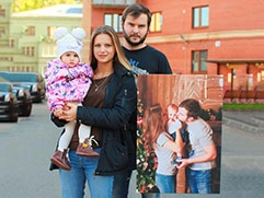 Муж, жена и ребенок с семейным фото на холсте, напечатанном и натянутом на подрамник, по фотографии, где они запечатлены вместе.