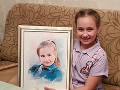 На фото изображена девочка, которая сидит на диване с узором, на ней надета светло-фиолетовая рубашка с рисунком, она держит в руках портрет на холсте в белой рамке; на портрете она сама, с улыбкой, в синей одежде, портрет выполнен в акварельном стиле.