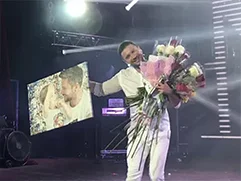 Сергей Лазарев на сцене с фотомозаикой, напечатанной для него на холсте.