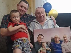 На фото изображена семейная сцена: пожилой мужчина, который держит в руках портрет по фото в стиле под масло, напечатанный на холсте, на портрете изображены он сам, еще один дедушка, его сын и внук; рядом с мужчиной сидит его сын и внук; на заднем плане видны воздушные шары.